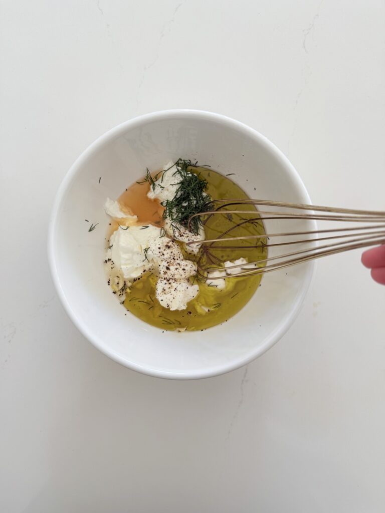 All ingredients together to make creamy Greek yogurt dressing in a white mixing bowl on the counter.