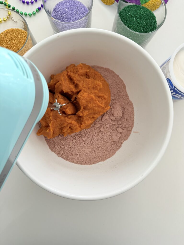 Cake batter and pumpkin puree are mixed in a large bowl on the counter.