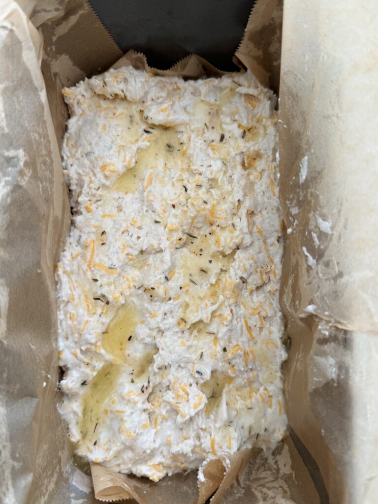 Dough drizzled with butter in a greased and parchment-paper-lined 9x5 loaf pan on the counter.