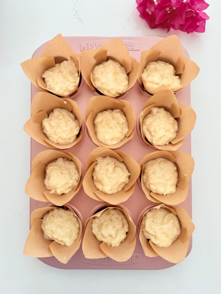 Batter in muffin cups in a pink muffin tin on the counter.