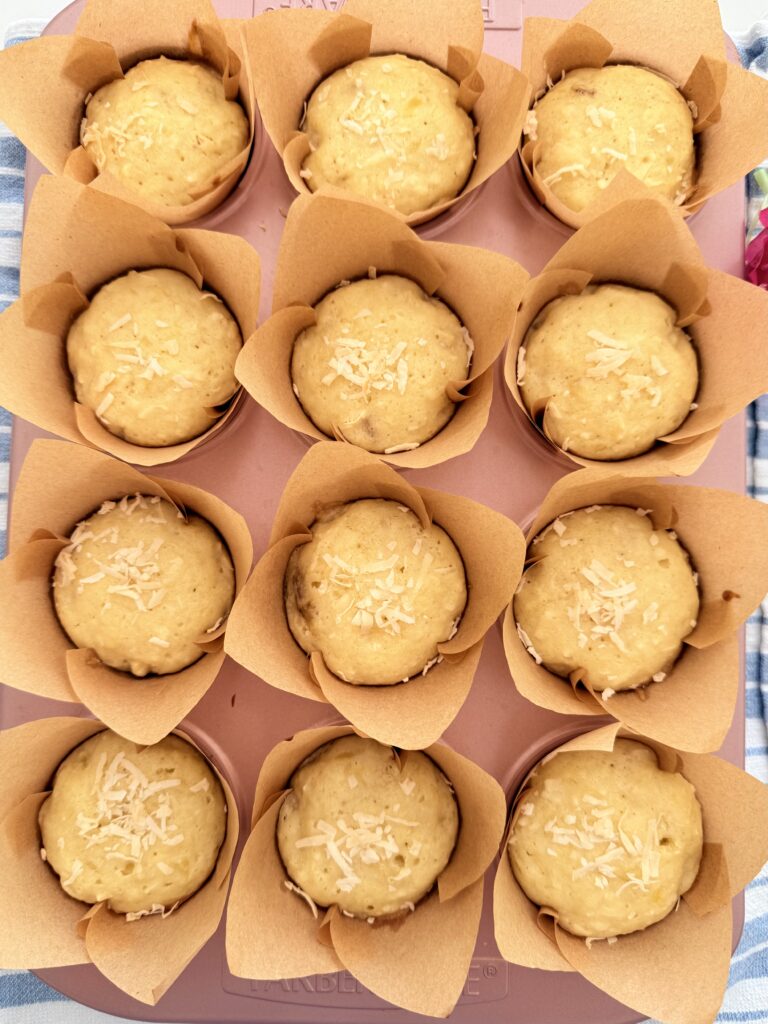 Fully baked Hawaiian Banana Muffins sprinkled with coconut on a blue and white towel on the counter.