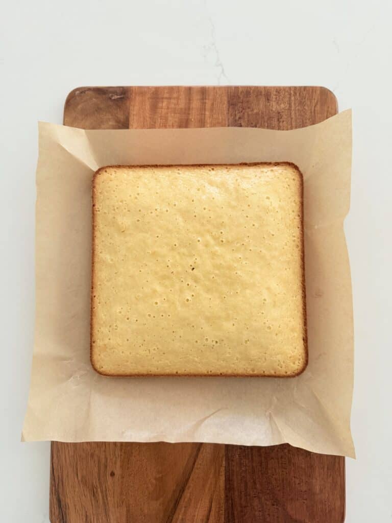 Unfrosted Almond Afternoon Cake on parchment paper on a brown cutting board.