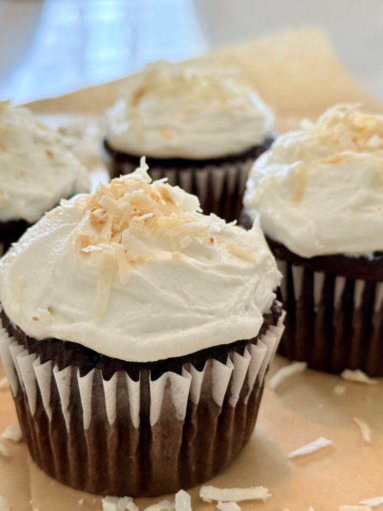 coconut buttercream on top of chocolate cupcakes on the counter.