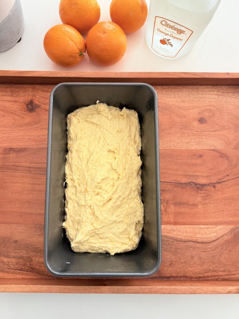 Batter put in a loaf pan on a brown tray on the counter.