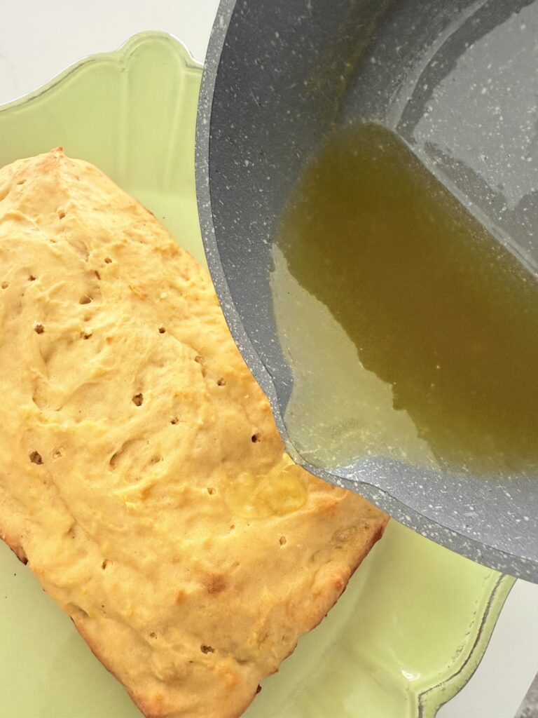 Cooked citrus lovers cake with holes in the cake so that syrup can be poured into the cake on a green cake platter on the counter.