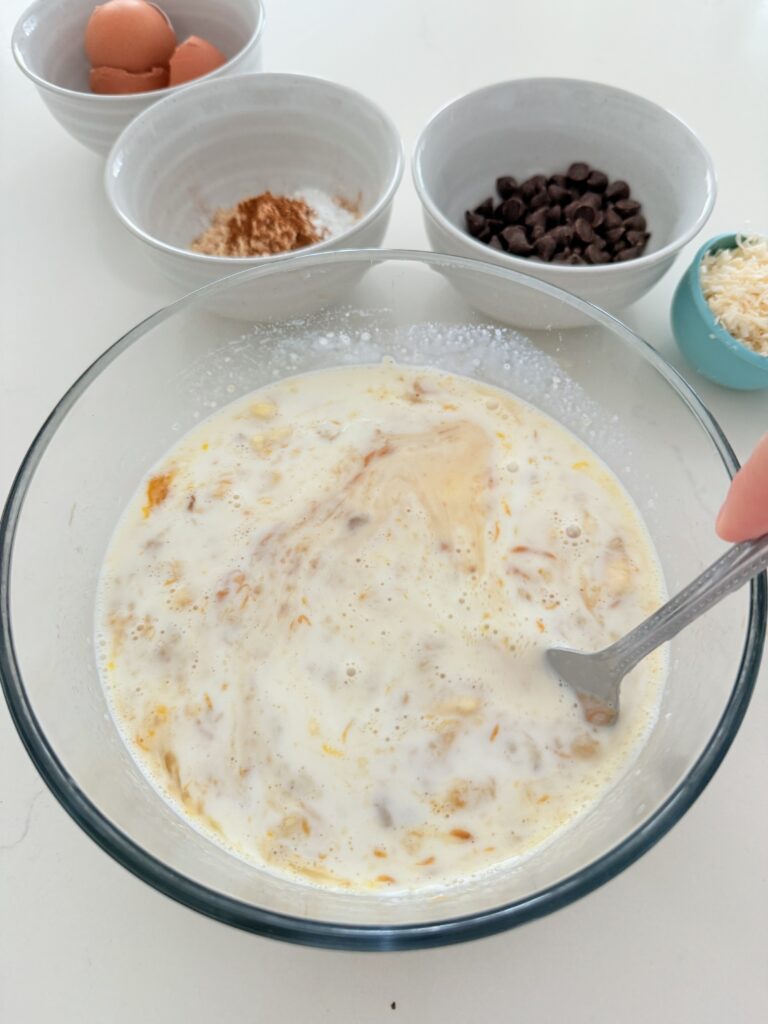 Mixing together mashed banana with wet ingredients in glass bowl on the counter.