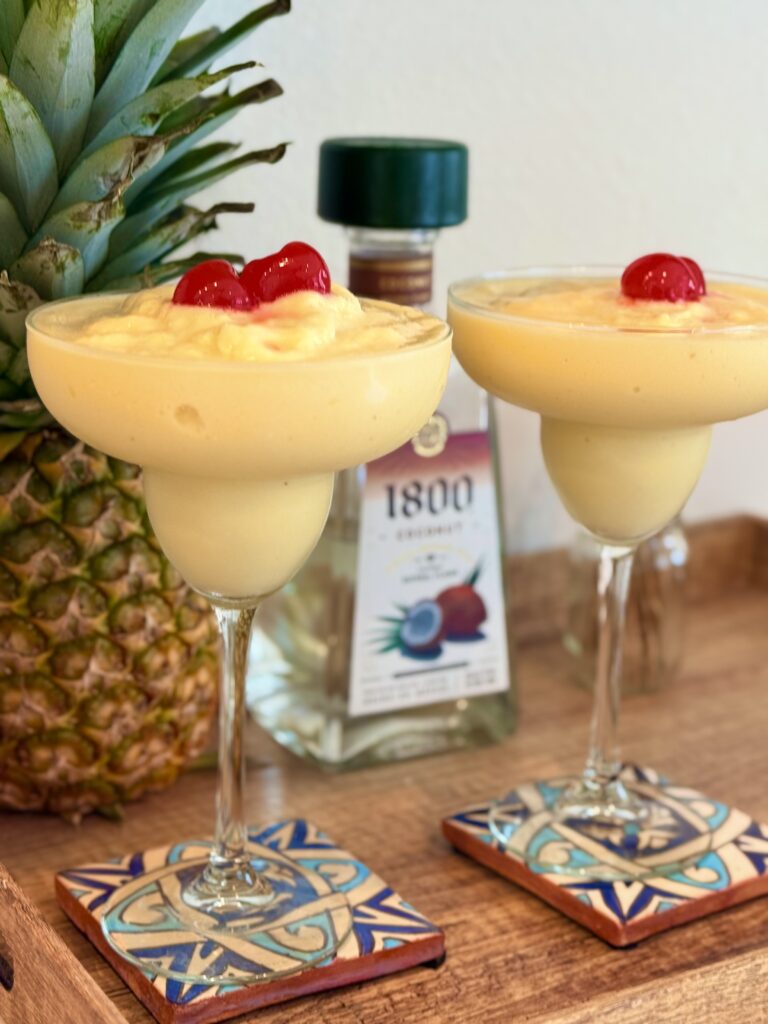 Two frozen pineapple, coconut margaritas on a brown tray on the counter.