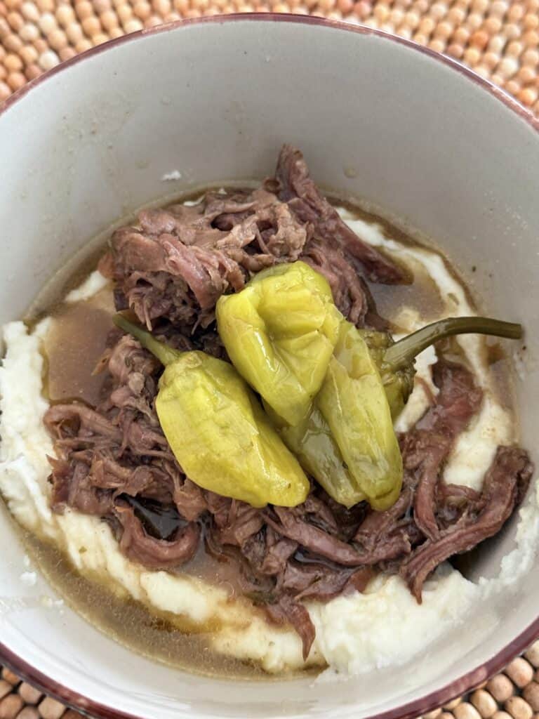 The slow cooker meat in a bowl topped over mashed potatoes on the counter.