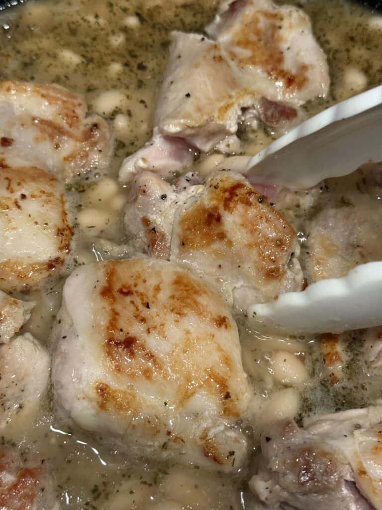 Using tongs and removing the brown pieces of chicken thigh from the pot on the stove top.