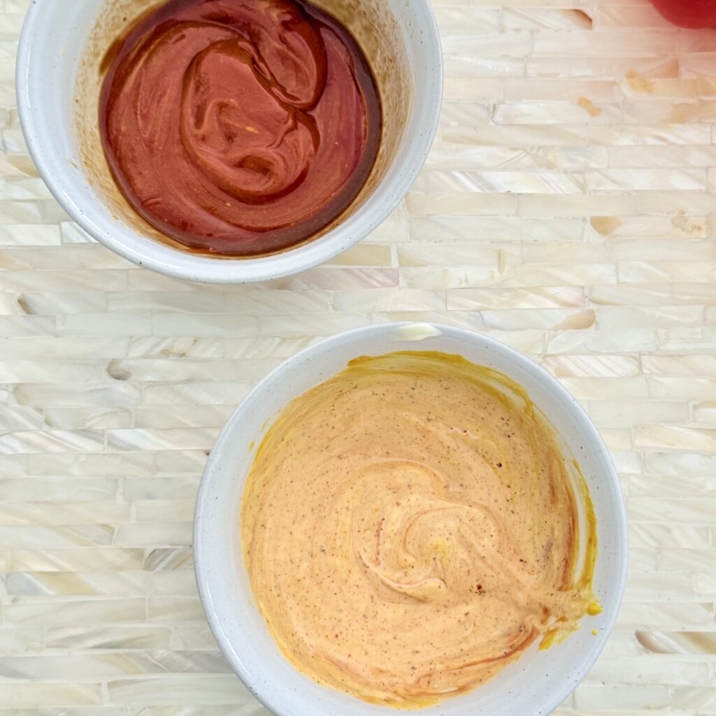 Mixed together, mustard, ketchup, mayo, and spices are in a small white bowl on a tray on the counter. Beside it is another small white bowl that has the mustard, ketchup, and Worcestershire sauce on a tray.