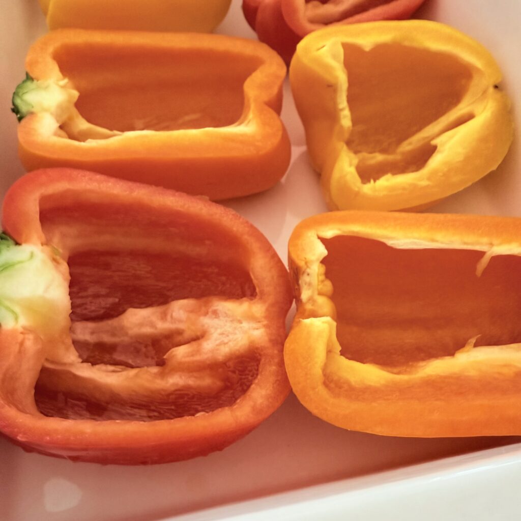 The peppers are sliced with their tops off and scooped out of the seeds. They are then placed upright in a 9x13-inch baking dish on the counter.