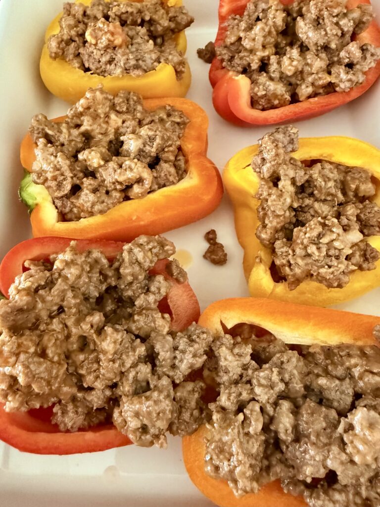 Raw bell peppers in a white baking dish, stuffed with meat and cheese on the stovetop.