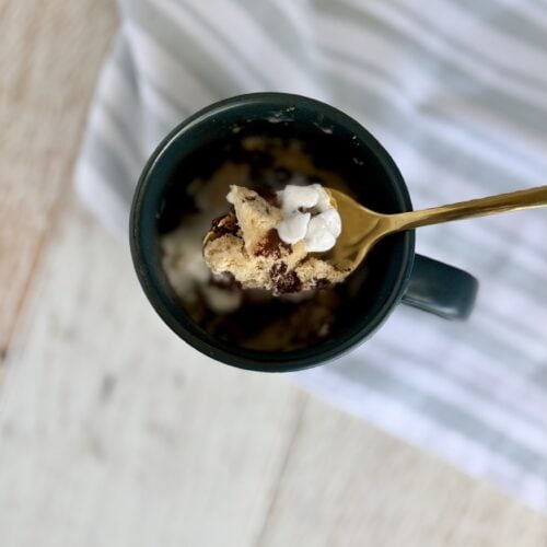 Close-up of a chocolate chip muffin in a mug with whipped cream and a gold spoon, perfect for quick dessert or breakfast.
