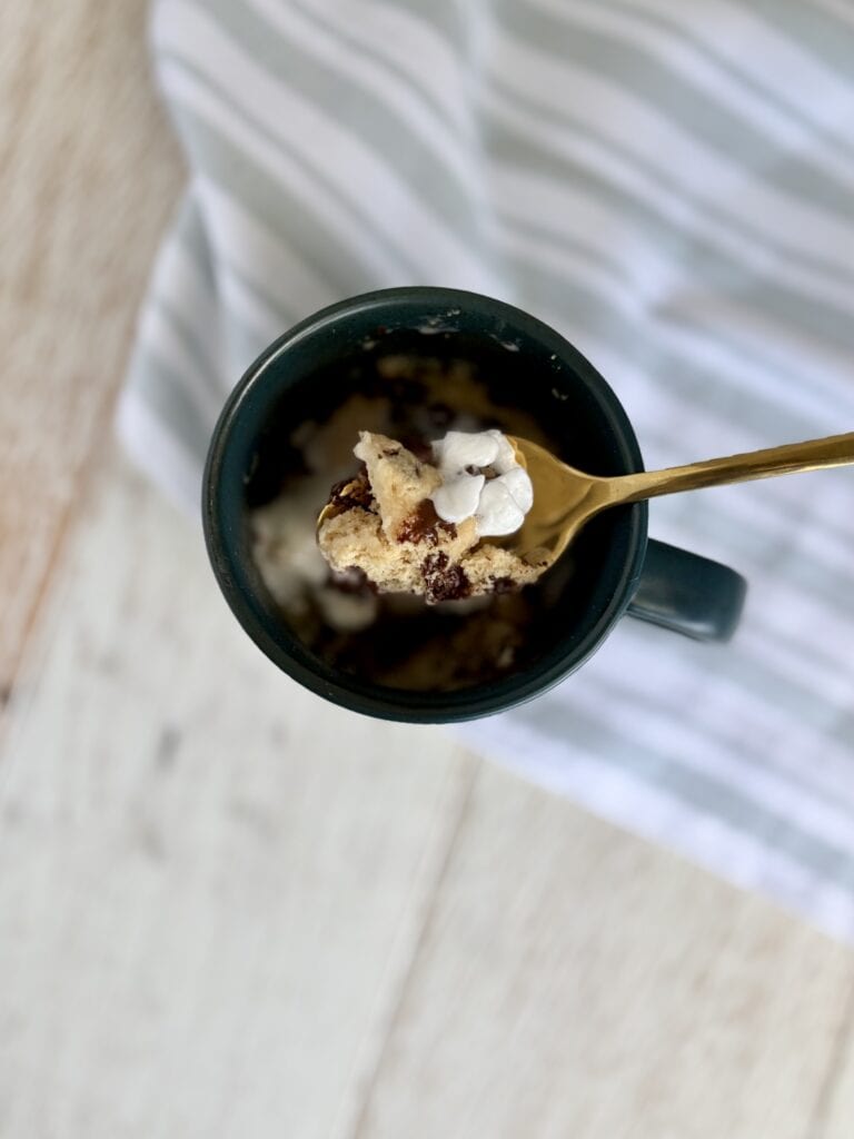Close-up of a chocolate chip muffin in a mug with whipped cream and a gold spoon, perfect for quick dessert or breakfast.