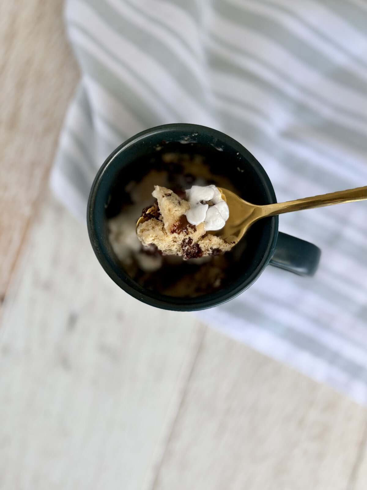 Close-up of a chocolate chip muffin in a mug with whipped cream and a gold spoon, perfect for quick dessert or breakfast.