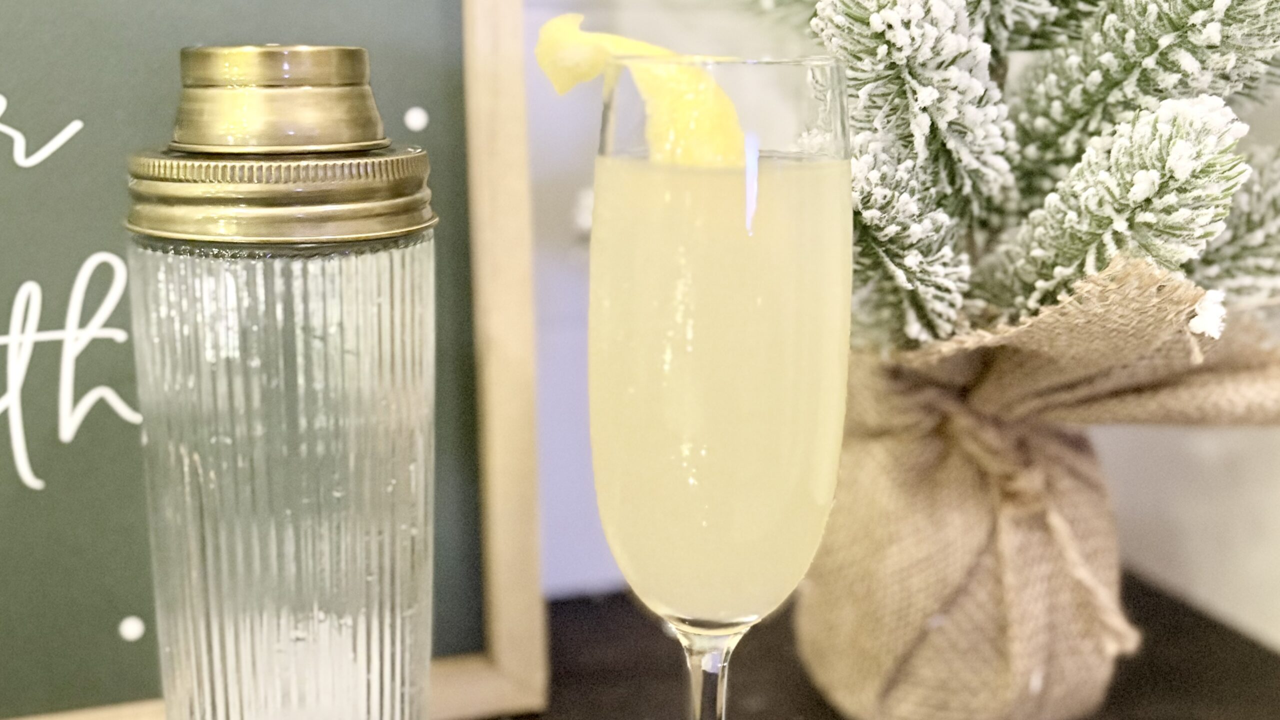 French 75 cocktail in a champagne glass next to a cocktail shaker on a counter