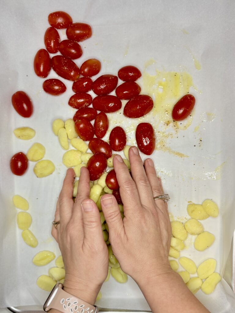 two hands mixing tomatoes and gnocchi with olive oil and seasoning 