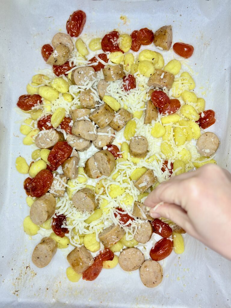 a hand sprinkling cheese over cooked and sliced sausage and gnocchi