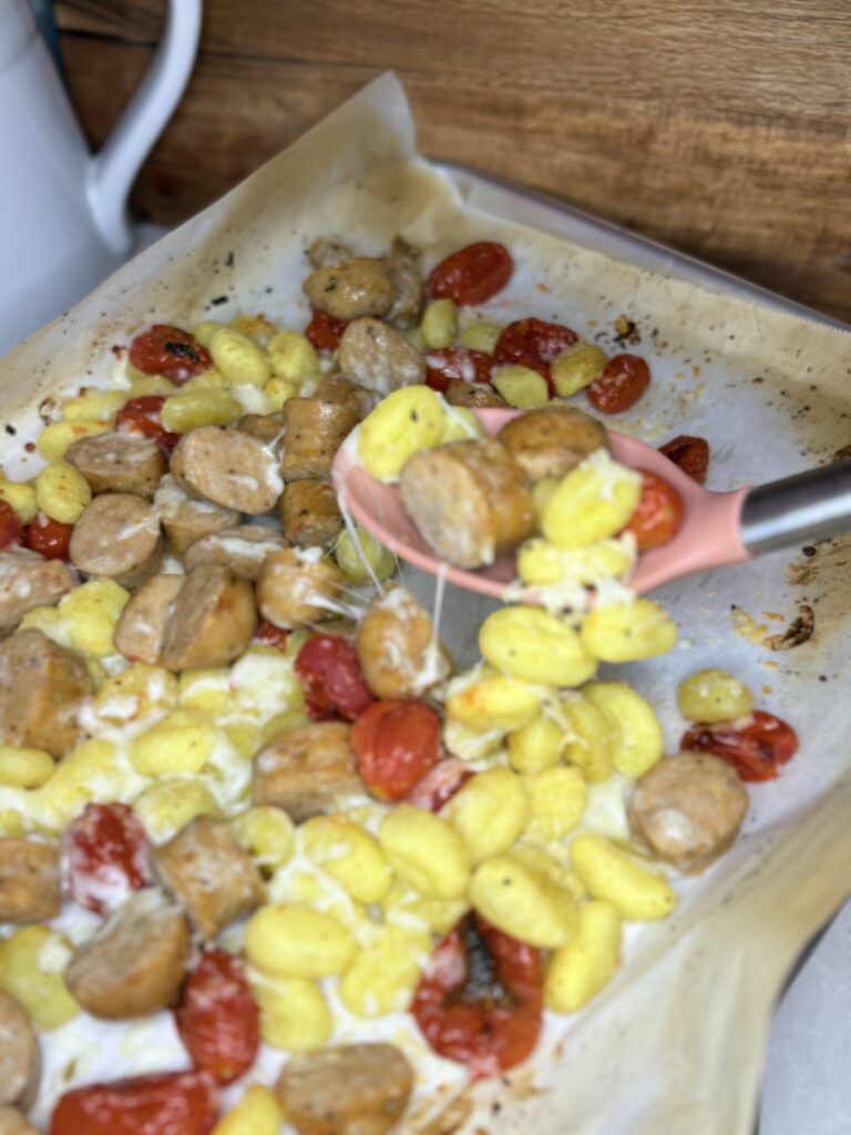 Italian sausage and Gnocchi on a sheet pan being scooped up with a spoon