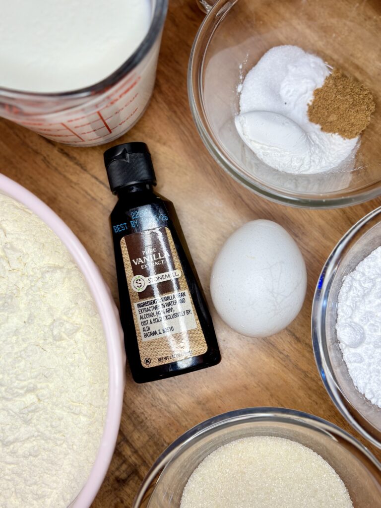 flour, buttermilk, baking powder, baking soda, salt, nutmeg, vanilla extract, egg, powdered sugar, granulated sugar on a wooden board