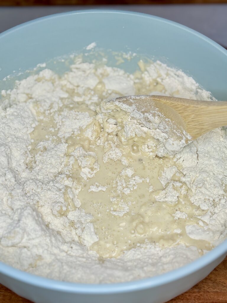 Dry ingredients being stirred into wet ingredients in a bowl with a wooden spoon