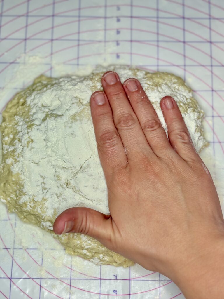 a hand flattening dough sprinkled with flour into a rectangle