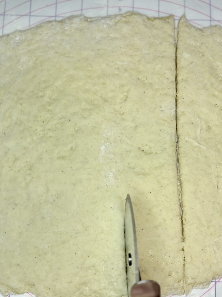 beignet dough being cut into squares with a pizza cutter