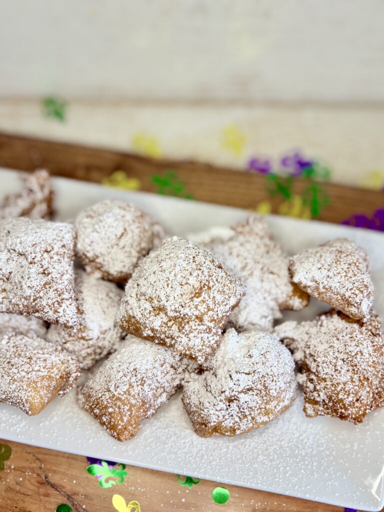 fried beignets on a plate sprinkled with powdered sugar