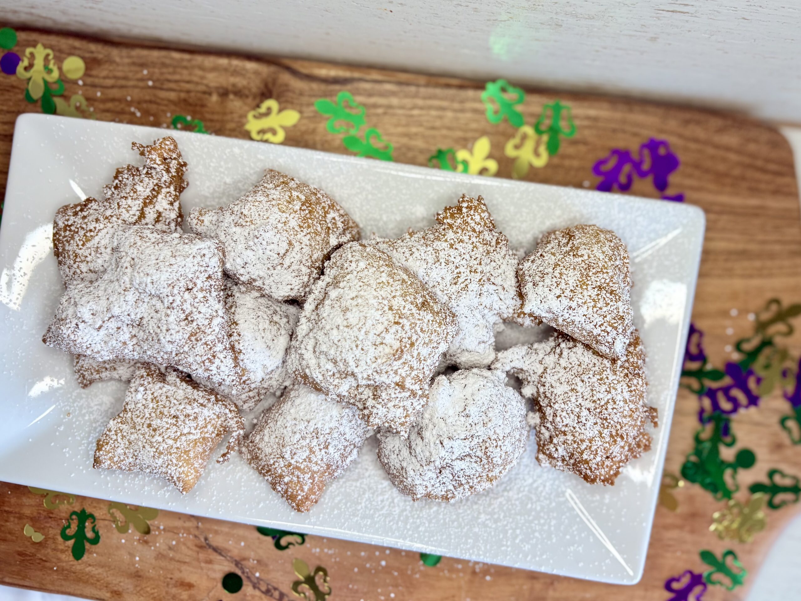 easy no yeah beignets on a plate on a cutting board with Mardi Gras confetti