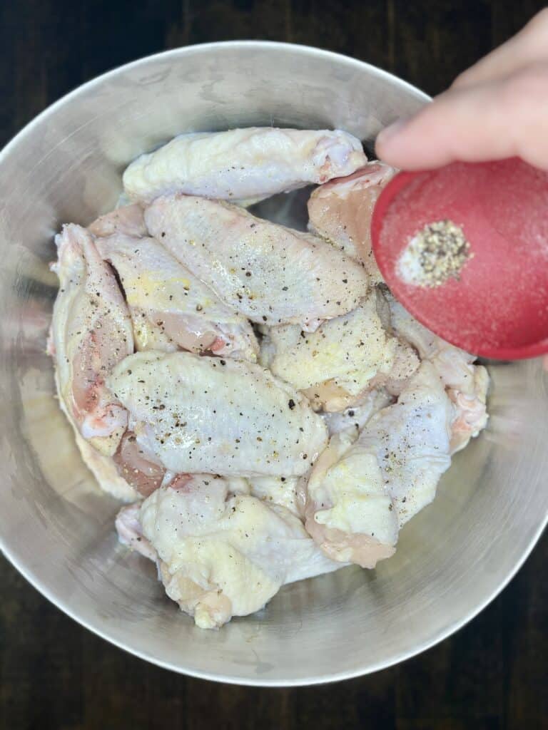 raw chicken wing pieces being sprinkled with salt and pepper