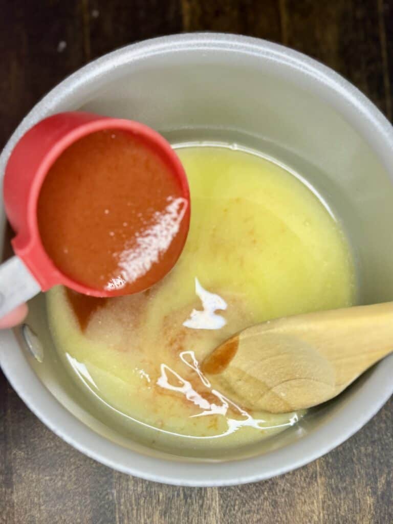 hot sauce being poured into a small sauce pan with  melted butter