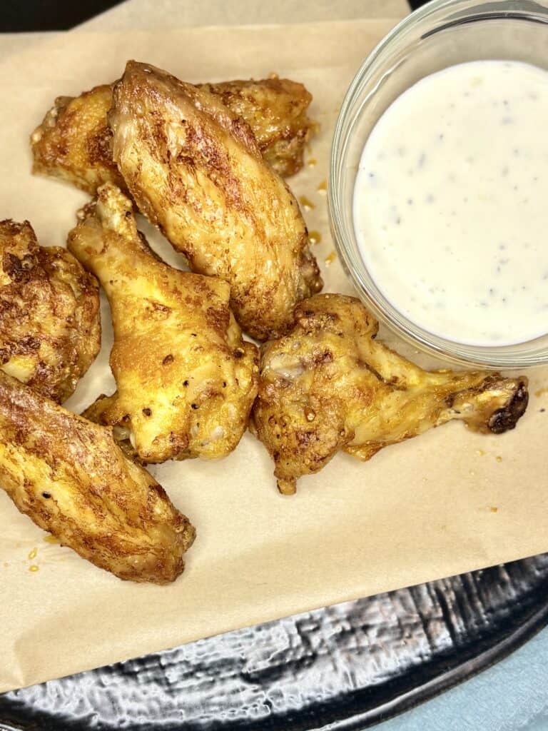 air fried buffalo wings on parchment paper next to a small bowl of dressing