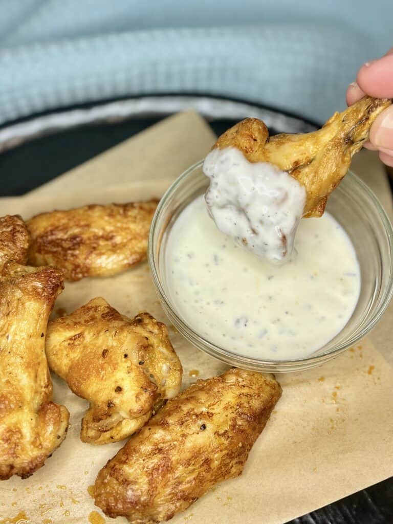 dry chicken wings on a plate with one being dipped into ranch dressing