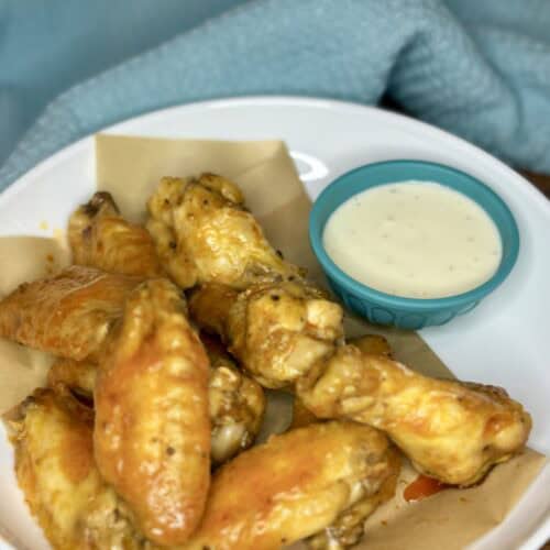 chicken wings coated in buffalo sauce on a plate next to a bowl of blue cheese dressing