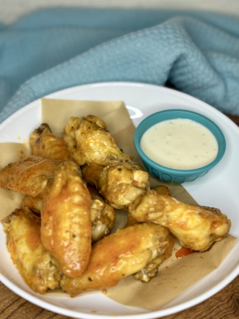 wet chicken wings coated in buffalo sauce on a plate next to a bowl of blue cheese dressing