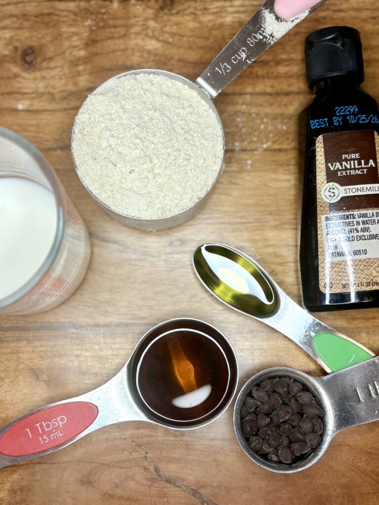 pancake mix, milk, oil, syrup, chocolate chips  in measuring cups with vanilla extract on a cutting board