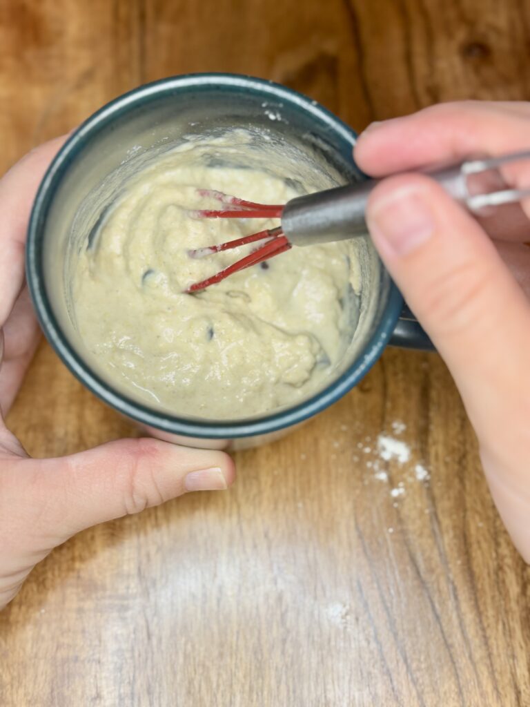 a hand whisking wet ingredients into dry ingredients in a mug