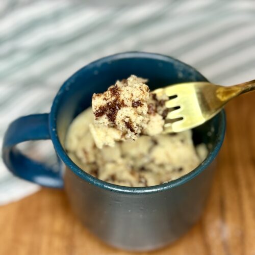 cooked chocolate chip muffin in a mug with a fork scooping up a bite