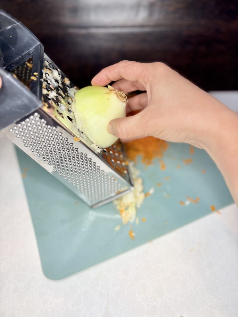 a hand grating an onion with a box grater over a cutting board