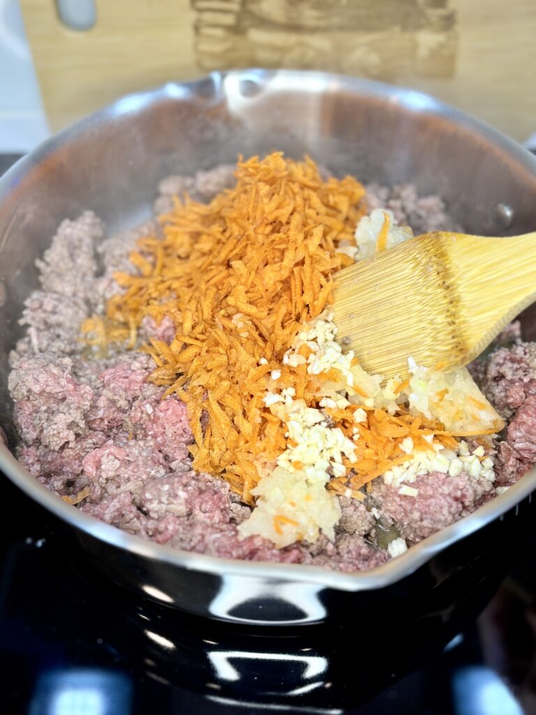 beef browning in a pan with grated carrots an onion 