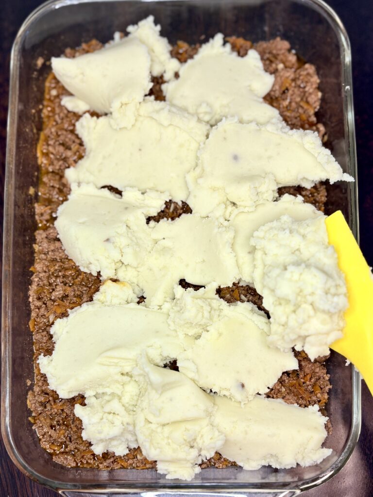 ground beef mixture in a baking dish with dollops of mashed potatoes over top