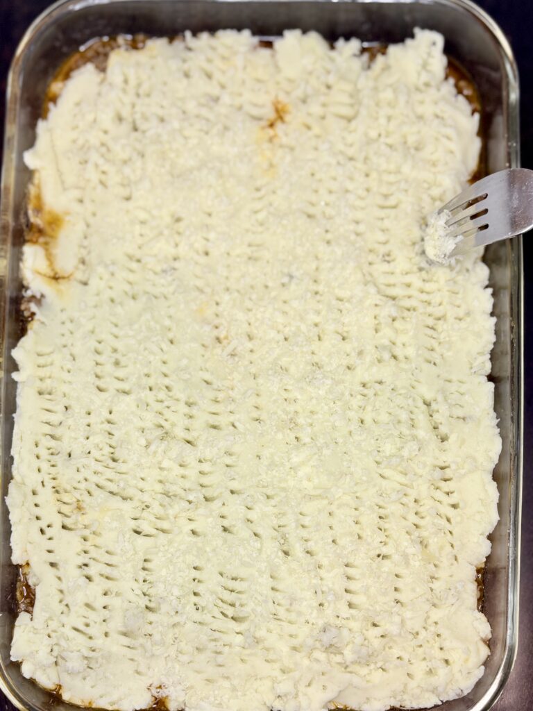 mashed potato layer over ground beef mixture being pricked with a fork to add texture