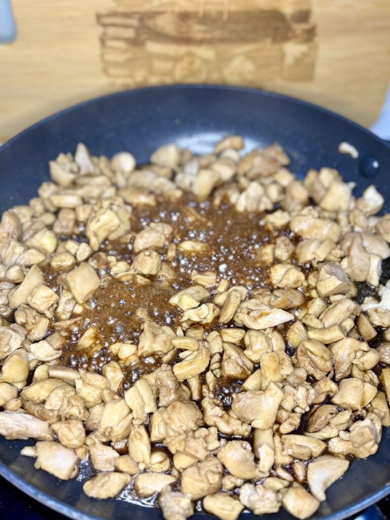 chicken being cooked in a pan with soy sauce and brown sugar bubbling up