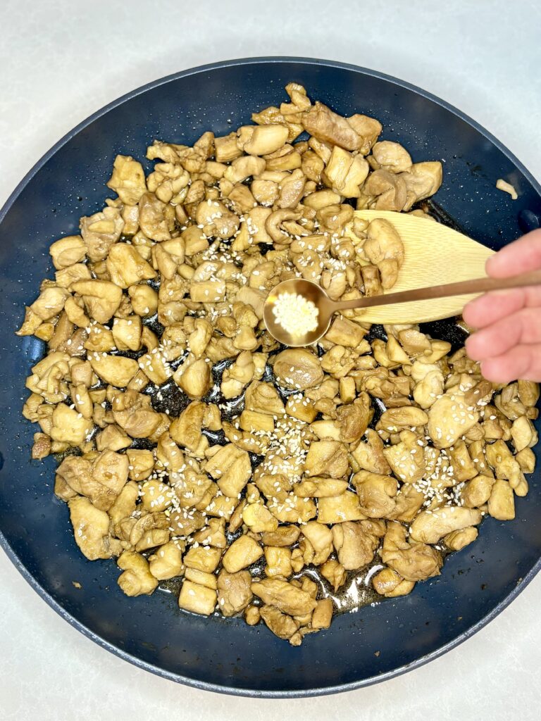 chicken teriyaki in a pan being sprinkled with sesame seeds