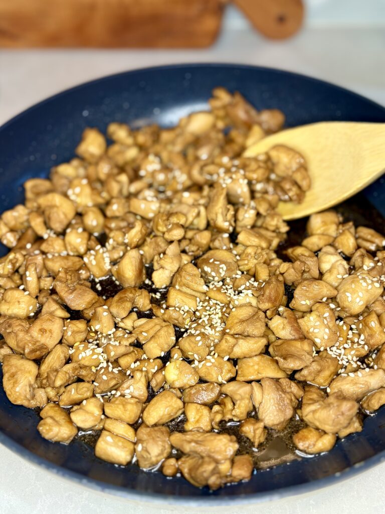 chicken teriyaki in a pan sprinkled with sesame seeds being scooped up with a wooden spoon