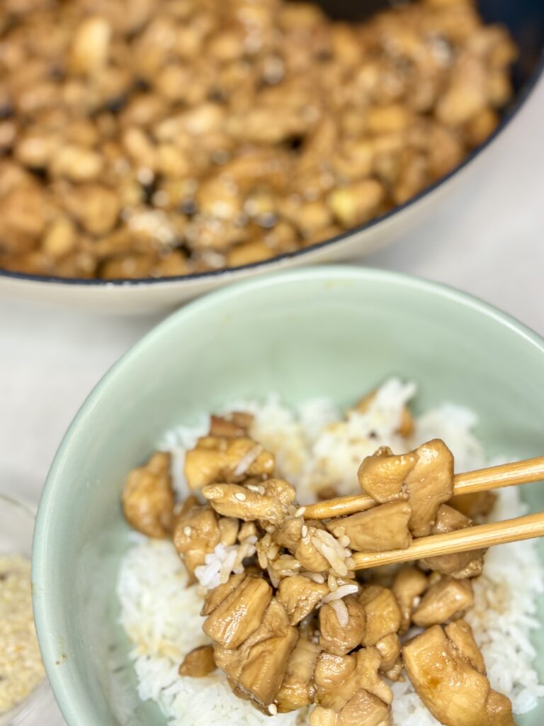 chicken and rice in a bowl being picked up with chopsticks next to a pan of chicken teriyaki