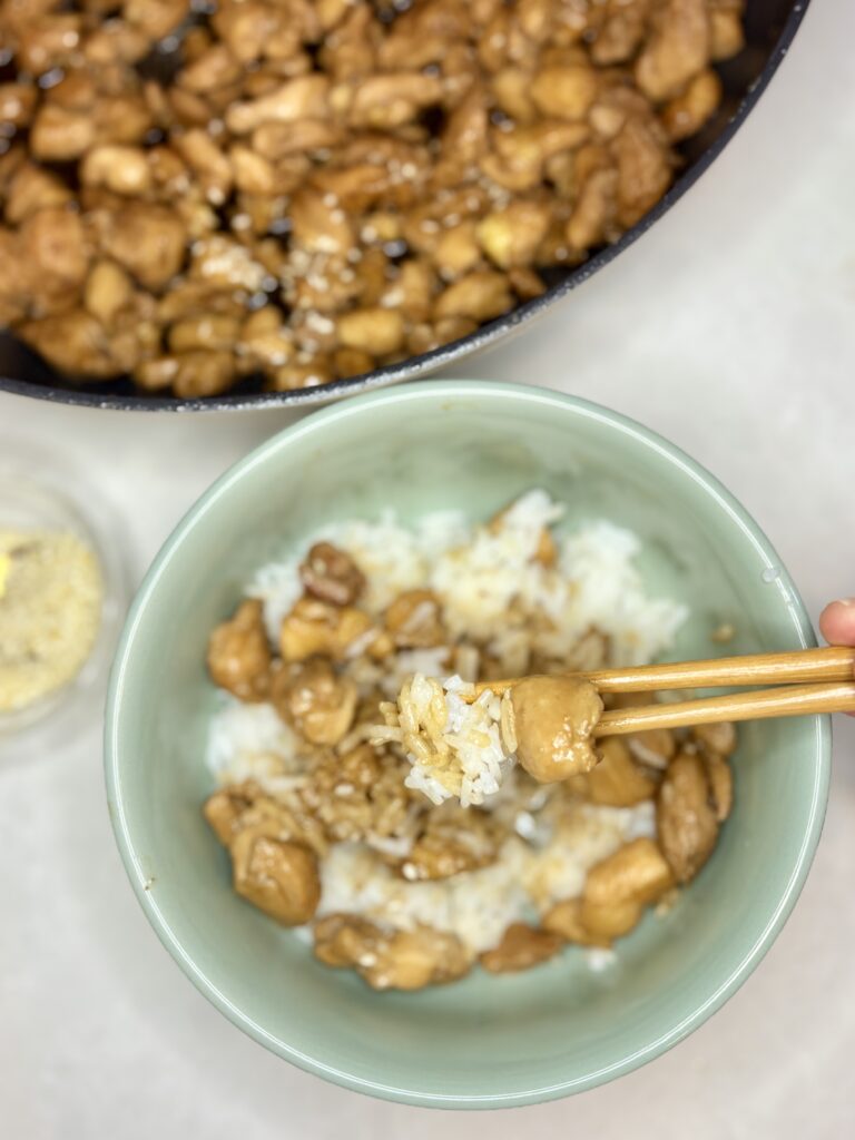 chicken and rice in a bowl being picked up with chopsticks next to a pan of chicken teriyaki