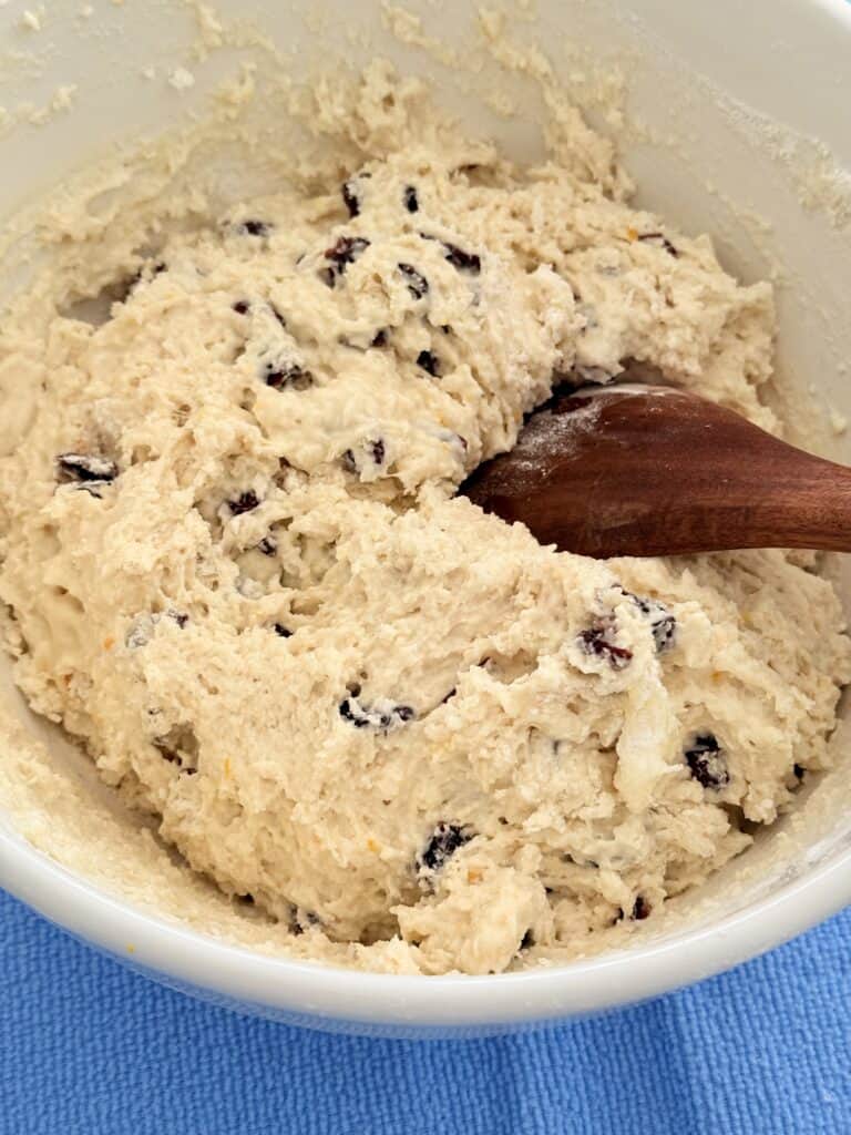 A wooden spoon mixing all of the ingredients in a large mixing bowl that is white on the counter.