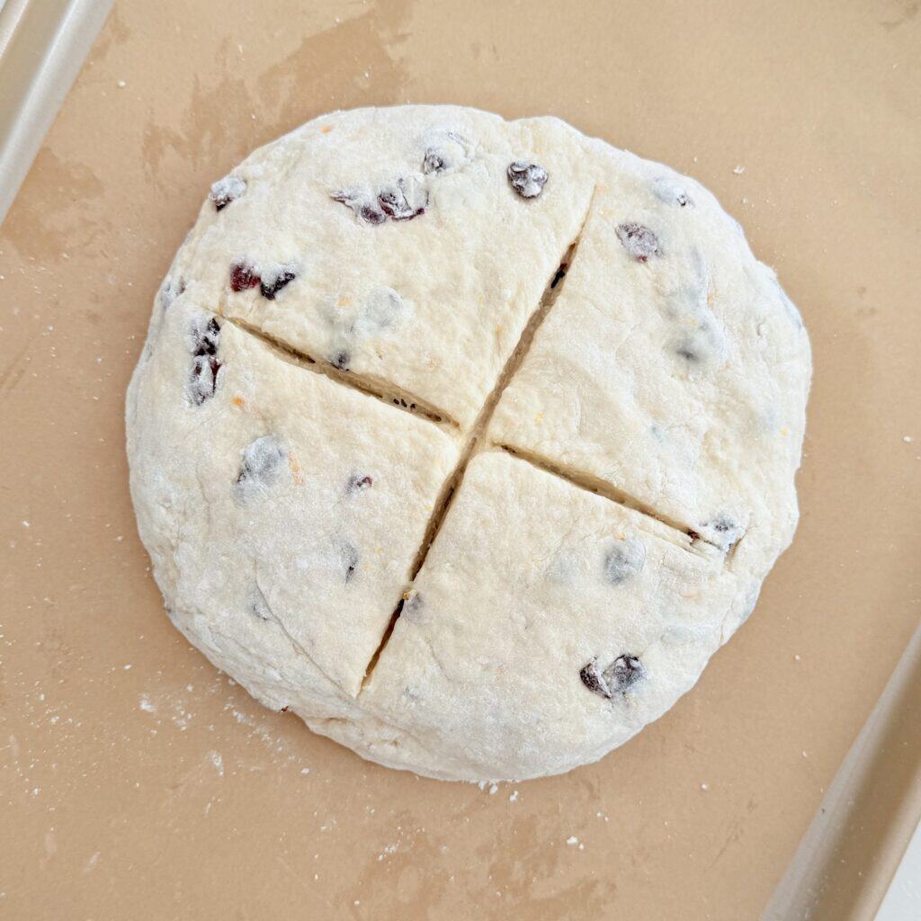 Unbaked Cranberry Orange Irish Soda Bread with an "X" cut on top of the dough on a parchment paper lined baking sheet on the counter.