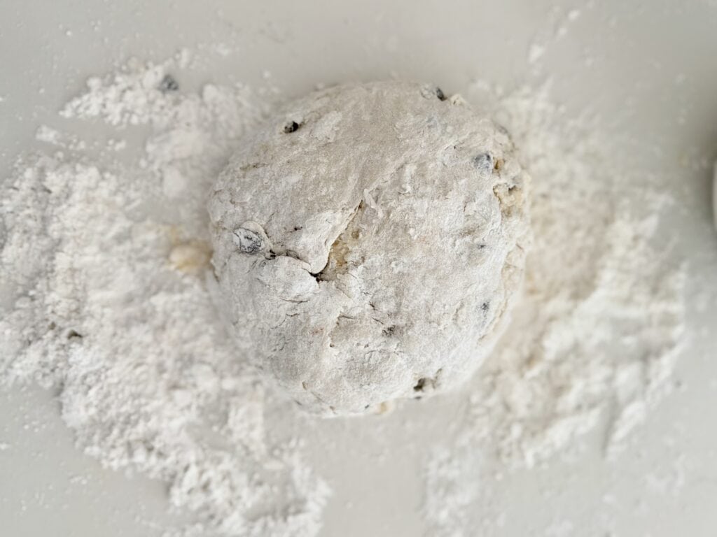 Dough on top of the white counter, sprinkled with flour on the counter and on top of the bread needing to be kneeded and rolled.